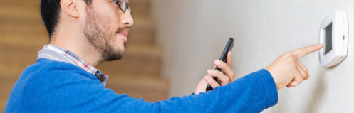 A man setting his smart thermostat by his phone.